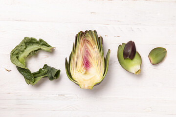 Half of purple raw roman artichokes on a white wooden table top view. Fresh italian vegetables