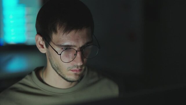 Closeup of a male programmer in glasses, focused on coding and problem-solving in a modern office environment.