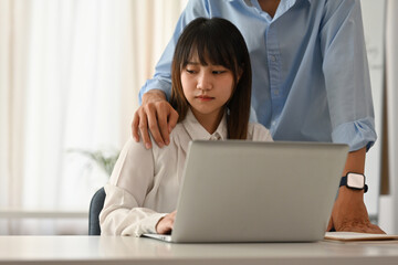A young woman appears uncomfortable as a male colleague places his hand on her shoulder. the issue...