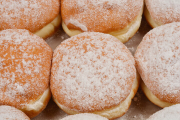 A detailed overhead shot of freshly baked doughnuts sprinkled with powdered sugar, arranged in rows on a light surface