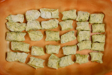 An overhead shot of raw potato and arugula gnocchi, arranged in a rectangular pattern on the bottom of a brown baking dish