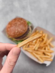 Hand holding french fry with hamburger and fries in background galentines day