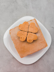 Delicious square cake decorated with heart shaped cookies forming a four leaf clover on white plate St. Patrick Mothers galentines day