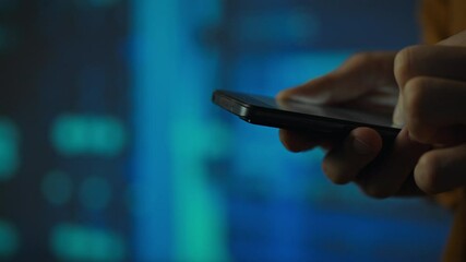A server room worker works with a smartphone holding it in his hands looking at the touch screen. Close-up of the hands of an engineer who is in the server room