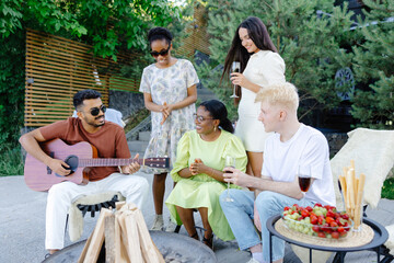 Friends celebrating together in summer at a picnic with wine and guitar