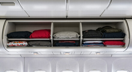 Fototapeta premium Neatly packed clothes in an airplane overhead compartment with a light background 