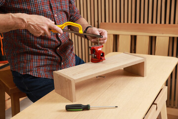 Relaxing hobby. Senior man with hacksaw and vise assembling wooden shelf in workshop, closeup