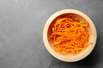Fresh orange zest in bowl on grey textured table, top view. Space for text