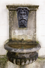 Stone Fountain with Grotesque Face Carving on Building Wall

