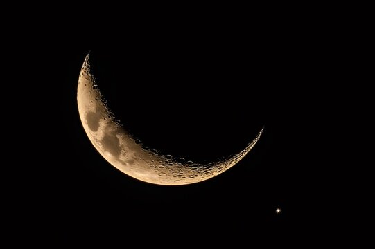 Waxing crescent moon glowing softly in the night sky, craters and a bright star are visible - Powered by Adobe