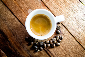 Overhead shot of espresso in a white cup on rustic wood table. Coffee beans form a curve near the cup. Warm, inviting morning vibe
