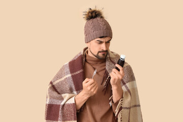 Ill young man with cough syrup on beige background