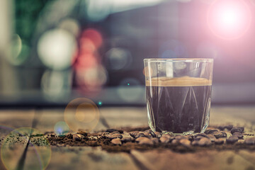 Espresso in a clear glass on a rustic wood surface. Coffee beans and grounds scattered around. Soft, blurred background with bokeh lights. Warm, inviting atmosphere.