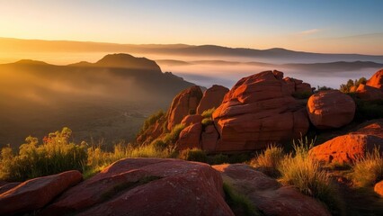 Breathtaking view of red rock cliffs at sunrise, with mist covering the valley below and lush grass in the foreground under a vibrant sky