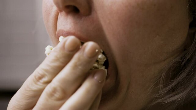 Woman stuffs mouth full submissively captivated by movie in cinema