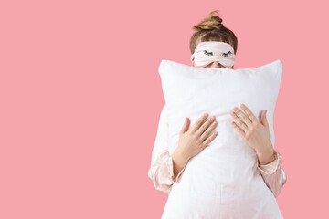Portrait of pretty young woman in pajamas with pillow on pink background