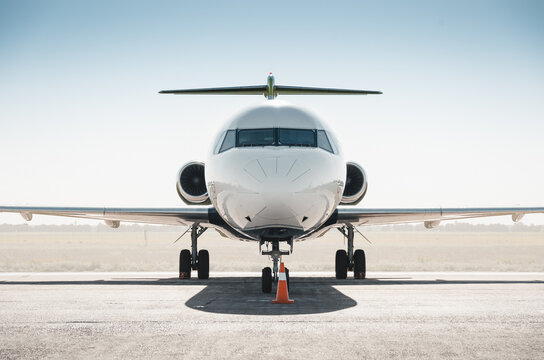 White passenger regional jet facing the camera. Symmetric frontal close-up view of passenger T-tail plane on a ground on a sunny day - bright afternoon sun shining in vertical direction.
