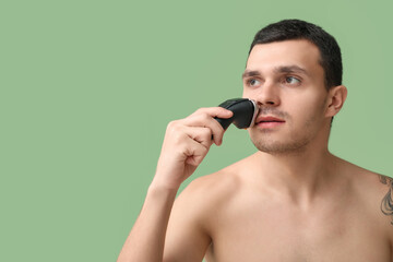 Handsome young man with electric shaver on green background