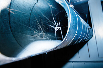 A close-up view inside a neglected ventilation pipe reveals a dense web of spiderwebs, highlighting...