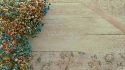 A flat lay of dried flowers in soft hues against a textured, rustic wooden background with floral patterns and pastel tones.