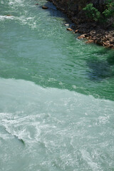 Obraz premium confluence of two rivers of different colors, emerald green and turquoise muddy water, riverside