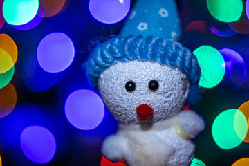 Very colorful illuminated Christmas decorations, in the shape of a snowman, with a blue hat and a background of blurred colored lights