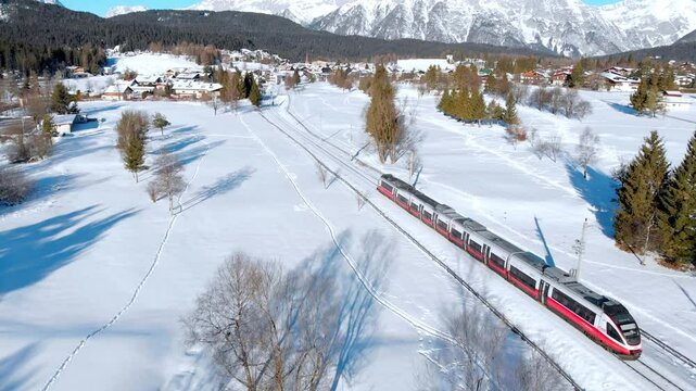 Aerial: Passenger train crossing a winter landscape in Seefeld in Tirol, Austria