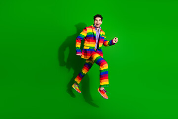 Young man joyfully jumps wearing a vibrant rainbow suit on a green background symbolizing pride, fun, and celebration