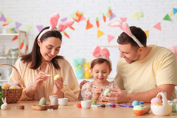 Happy family in bunny ears painting Easter eggs at home