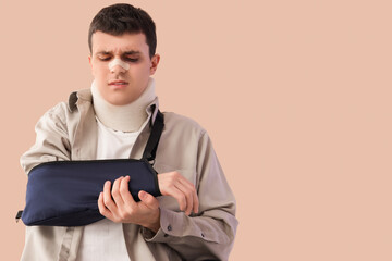 Injured young man after accident with broken arm on beige background