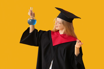 Female graduating student in mortar board with laboratory glassware on yellow background
