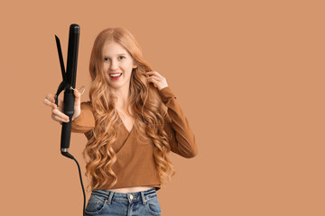 Beautiful young happy woman with curling iron on brown background