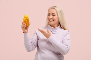 Mature woman showing bottle of fish oil pills on green background