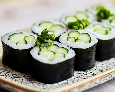 Close-up of cucumber sushi rolls on a patterned plate, showcasing fresh cucumber slices and rice, garnished with green onion, representing healthy Japanese cuisine and a refreshing meal