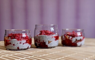 A lot of healthy Chia pudding with coconut milk in a glass containers in view can with fresh berries as raspberry, red currant, cranberry and pieces of peach on bamboo background. Close-up