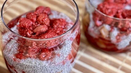 A lot of healthy Chia pudding with coconut milk in a glass containers in view can with fresh berries as raspberry, red currant, cranberry and pieces of peach on bamboo background. Close-up