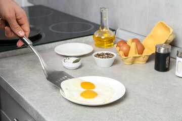 Man with frying pan putting tasty fried eggs onto plate in kitchen, closeup