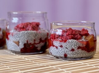A lot of healthy Chia pudding with coconut milk in a glass containers in view can with fresh berries as raspberry, red currant, cranberry and pieces of peach on bamboo background. Close-up