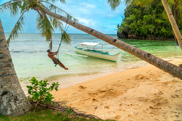 Tourist swinging from palm tree on kangbangyo island, siargao, philippines