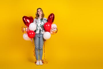 Young stylish woman holding colorful balloons against a vibrant yellow backdrop, depicting a...