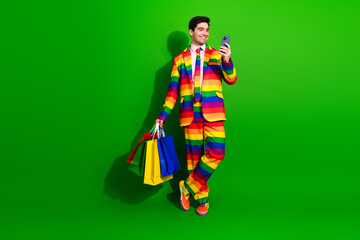 Young Handsome Man in a Rainbow Striped Suit Holding Shopping Bags Against a Vibrant Green...