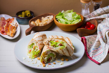 Turkey wraps on a plate and ingredients on a table. Tortilla, burritos, sandwiches, twisted rolls