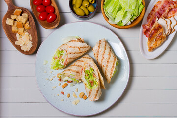 Turkey wraps on a plate and ingredients on a table. Tortilla, burritos, sandwiches, twisted rolls. High angle view