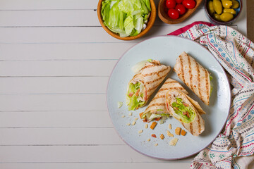 Turkey wraps on a plate and ingredients on a table. Tortilla, burritos, sandwiches, twisted rolls. High angle view with copy space