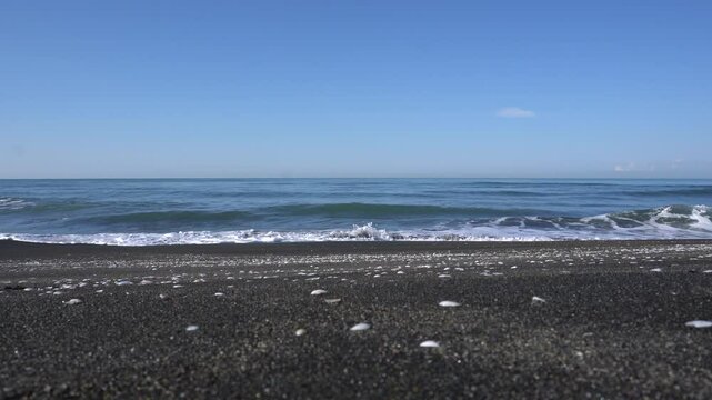 Scenic video from the Black Sea coast in Ureki, Georgia. The waves gently roll over the dark sandy beach, creating a relaxing atmosphere. Unique magnetic sand of Ureka glitters in the sun