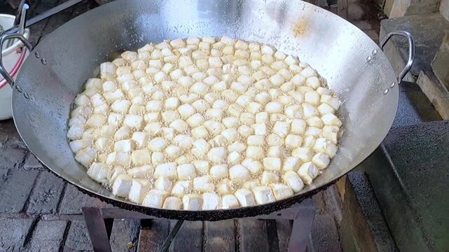 Cinematic shot. The cooking process of Tofu being deep-fried, likely for a dish called Crispy Pong Tofu, a popular Indonesian street food