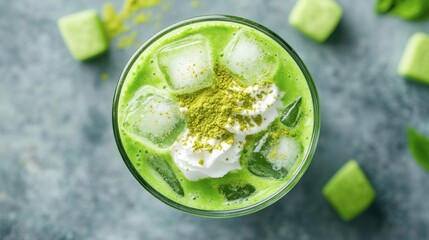Obraz premium Refreshing green tea frappe in a glass, seen from above, with ice cubes, whipped topping, and a dusting of matcha powder