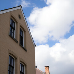 Fototapeta premium Gable with Windows of Old White Painted Stone Building against Blue Cloudy Sky