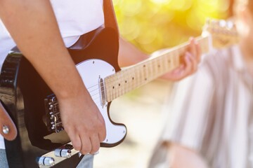 Young adult playing electric guitar outdoors in sunlit setting