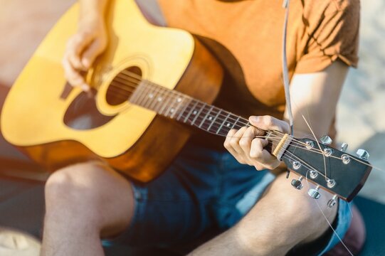 Young adult playing acoustic guitar outdoors in sunlight